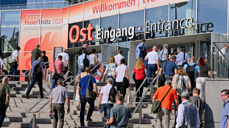 Besuchergruppe beim Betreten eines Messegebäudes durch den Ost Eingang, deutlich sichtbares Schild mit "Willkommen" und Datum der FeuerTrutz 2024 Veranstaltung.