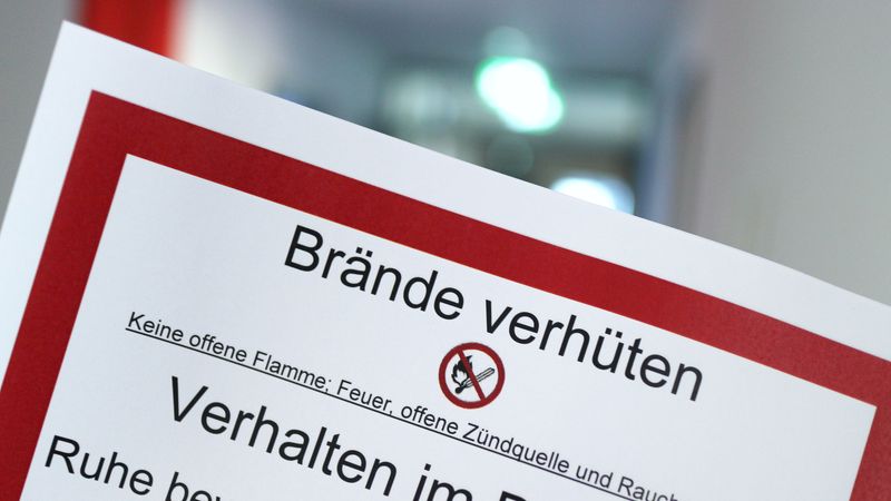 Die Nahaufnahme zeigt ein Schild mit dem Titel 'Brände verhüten', das die Verwendung von offenen Flammen verbietet und Verhaltenstipps im Brandfall gibt.