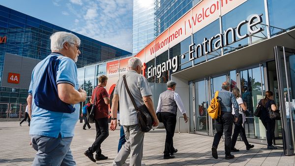 Besucher betreten den Eingang einer Messehalle bei sonnigem Wetter.
