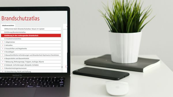 Ein Laptop auf einem Schreibtisch zeigt den Brandschutzatlas auf dem Bildschirm. Daneben stehen ein Smartphone, eine Maus und eine Pflanze.
